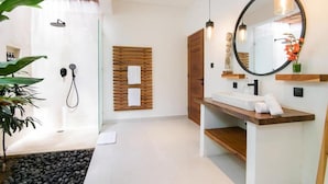 Een moderne badkamer met een douchecabine van glas, een houten wandpaneel, een houten wastafelmeubel en een ronde spiegel.