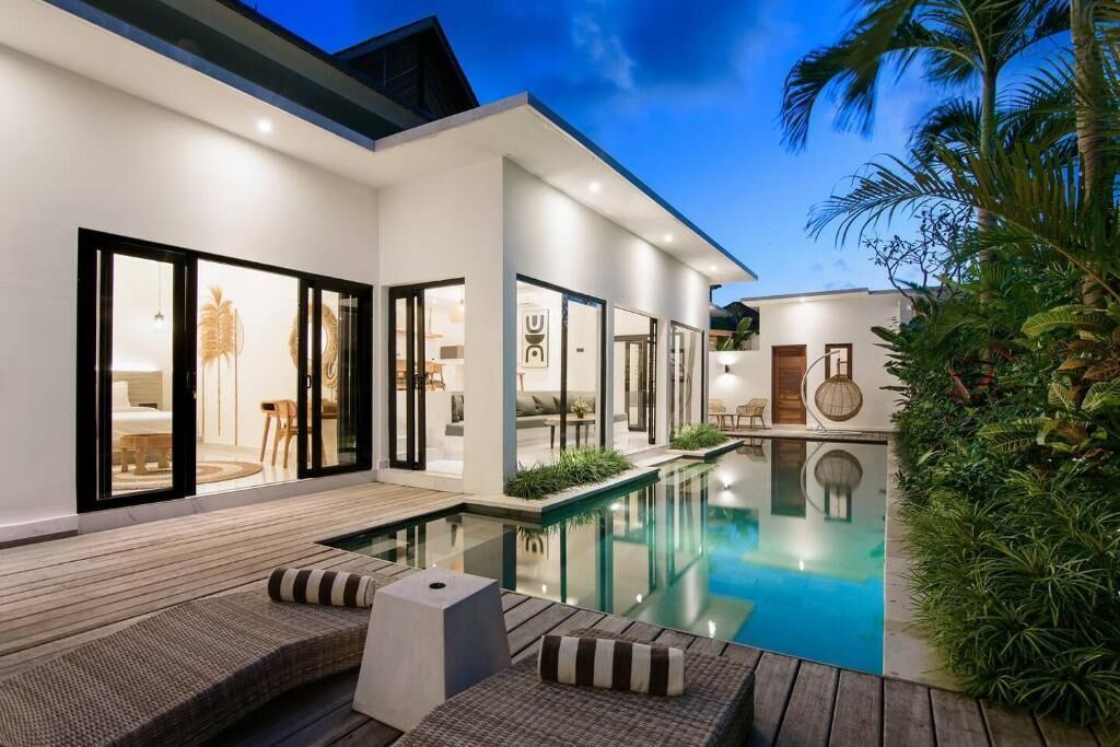 A modern house with a swimming pool, outdoor seating, and a well-lit interior.