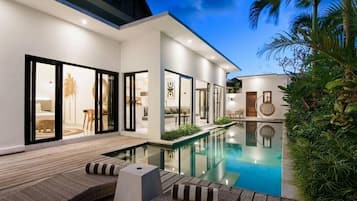 Ein modernes Haus mit Swimmingpool, Sitzgelegenheit im Freien und einem gut beleuchteten Innenraum.