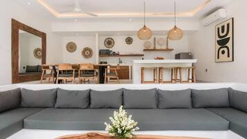 Un salon moderne avec un grand canapé gris, une table à manger en bois et des luminaires suspendus.