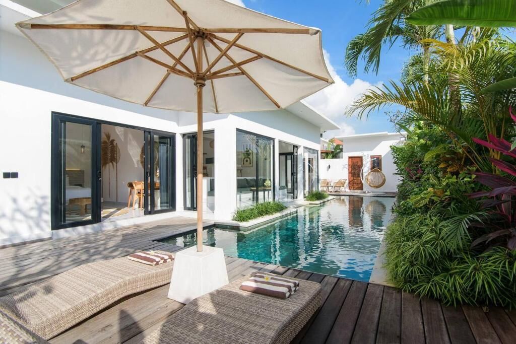 Un espace piscine extérieur moderne, doté d’une terrasse en bois, de chaises longues et d’un grand parasol.