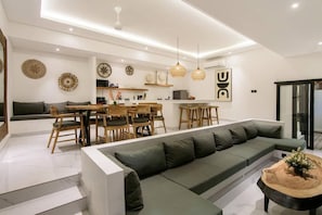 A modern living room with a sectional sofa, dining area, and kitchen in the background. - Lena Villa by Tasvan (Badung)