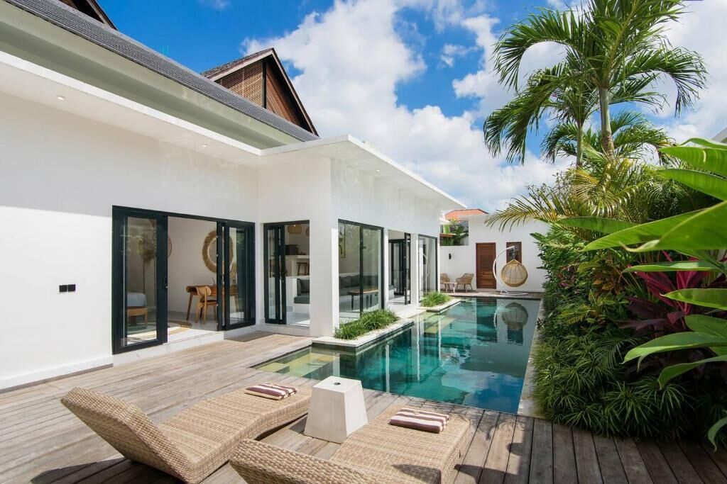 Una casa moderna con piscina, mobiliario exterior y abundante vegetación.
