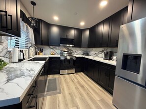 A modern kitchen with dark cabinets, a stainless steel refrigerator, a built-in oven, and a marble countertop. - Escape to the pines at Bow String Retreat (Munds Park)