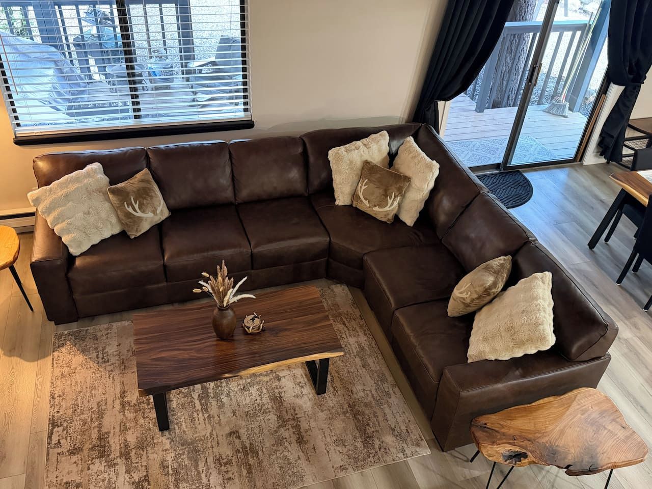 Ein braunes, ledernes Ecksofa mit Zierkissen, ein Couchtisch aus Holz mit einer Vase und ein rustikaler Teppich.