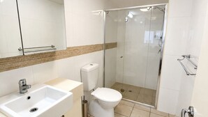 A modern bathroom with a white sink, toilet, and glass-enclosed shower. - River Glimpse 2BR Walk to CBD & Parking (Brisbane City)