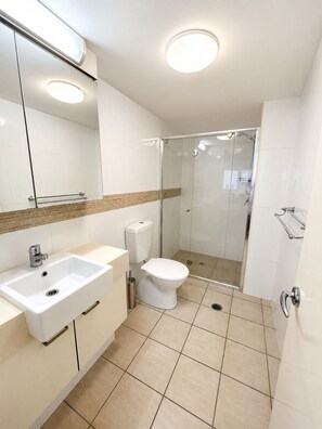 A modern bathroom with a white sink, toilet, and glass-enclosed shower. - River Glimpse 2BR Walk to CBD & Parking (Brisbane City)