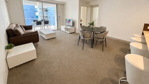 A modern living room with a sofa, a coffee table, a dining table with chairs, and a television. - River Glimpse 2BR Walk to CBD & Parking (Brisbane City)