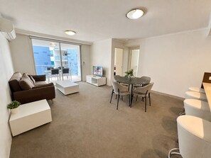 A modern living room with a sofa, a coffee table, a dining table with chairs, and a television. - River Glimpse 2BR Walk to CBD & Parking (Brisbane City)