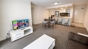 A modern living room with a flat-screen TV, a dining area with a table and chairs, and a kitchenette with cabinets and a countertop. - River Glimpse 2BR Walk to CBD & Parking (Brisbane City)