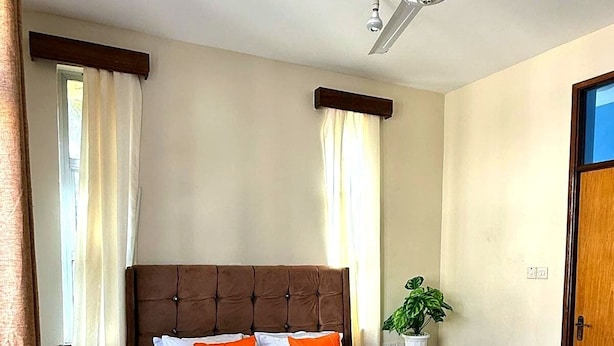 A bedroom with a large bed, a ceiling fan, a potted plant, and a door. - Pristine & Breezy 2BR Retreat with Pool, Gym & Balcony Views – Mtwapa Coast (Mtwapa)