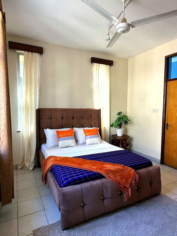 Quarto com cama grande, ventilador de teto, planta em vaso e porta.