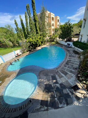 Piscina de borda curva, rodeada por azulejos de pedra e vegetação.