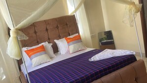 A four-poster bed with a canopy, a tufted headboard, and a checkered bedspread. - Pristine & Breezy 2BR Retreat with Pool, Gym & Balcony Views – Mtwapa Coast (Mtwapa)