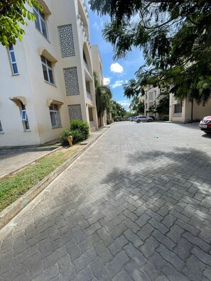 A paved street in a residential area with multi-story buildings, a clear sky, and parked cars. - Pristine & Breezy 2BR Retreat with Pool, Gym & Balcony Views – Mtwapa Coast (Mtwapa)