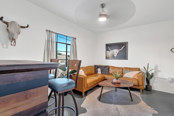 A modern living room with a brown leather sofa, a wooden bar counter, and a ceiling fan.