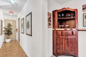 A hallway with framed artwork, a potted plant, and a wooden cabinet with glassware.