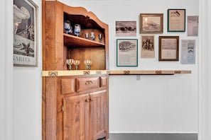 A wooden cabinet with wine glasses and a shelf above it.