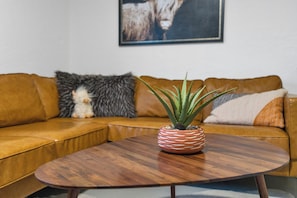 A living room with a brown leather sofa, a small potted plant on a wooden coffee table, and a framed picture on the wall.