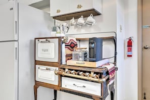 A kitchenette with a vintage stove, a coffee machine, and a set of white mugs on a shelf.