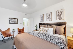 A bedroom with a bed, a chair, a nightstand, and wall art.