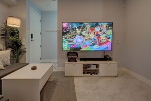 A modern living room with a flat-screen TV mounted on the wall, a white entertainment unit below, and a coffee table in the foreground.