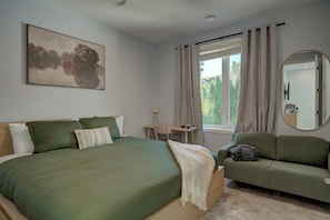 A bedroom with a bed, a sofa, a desk, a mirror, and a window with curtains.