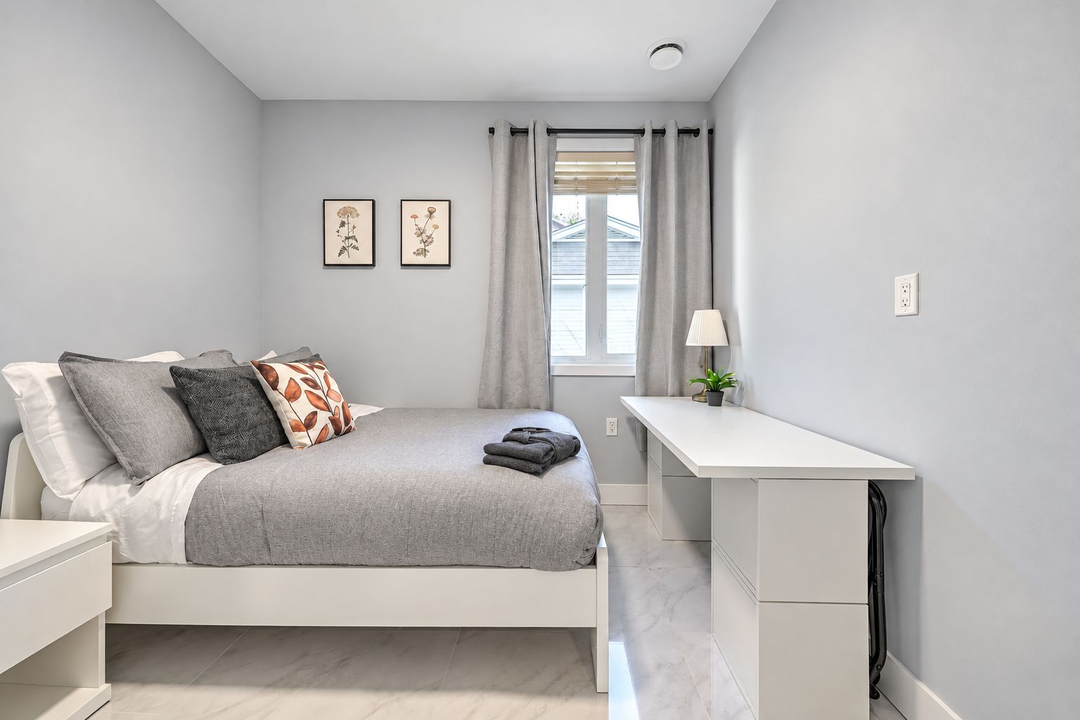 Ein modernes Schlafzimmer mit Bett, Nachttisch, Schreibtisch und einem Fenster mit Vorhängen.