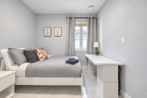 Un dormitorio moderno con cama, mesita de noche, escritorio y ventana con cortinas.