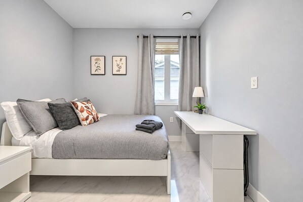 A modern bedroom with a bed, bedside table, desk, and a window with curtains. - Cozy 5-bedroom house in peaceful Vancouver perfect for families (Vancouver)