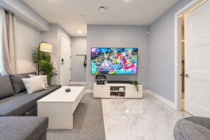 A modern living room with a flat-screen TV, a grey sofa, a white coffee table, and a minimalist design. - Cozy 5-bedroom house in peaceful Vancouver perfect for families (Vancouver)