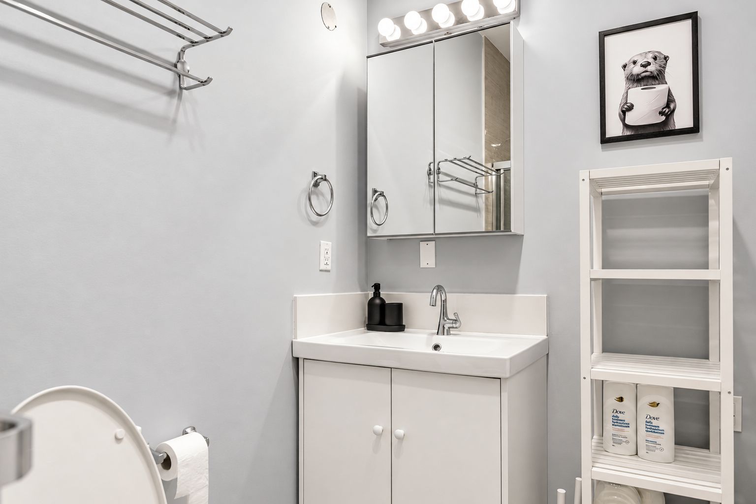 Une salle de bain avec un lavabo blanc, un miroir avec éclairage, un porte-serviettes et une étagère contenant des produits Dove.