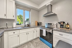 A modern kitchen with white cabinets, a stainless steel range, and a window with a view of greenery. - Cozy 5-bedroom house in peaceful Vancouver perfect for families (Vancouver)