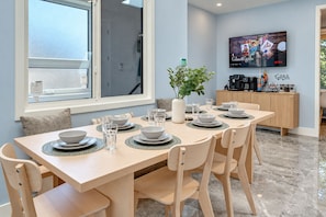 A dining area with a table set for six, a television mounted on the wall, and a view of the outdoors through a window. - Cozy 5-bedroom house in peaceful Vancouver perfect for families (Vancouver)