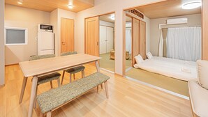 Una camera d'albergo con un tavolo da pranzo in legno, una panca e sedie, un letto con tende e un angolo cottura con forno a microonde.