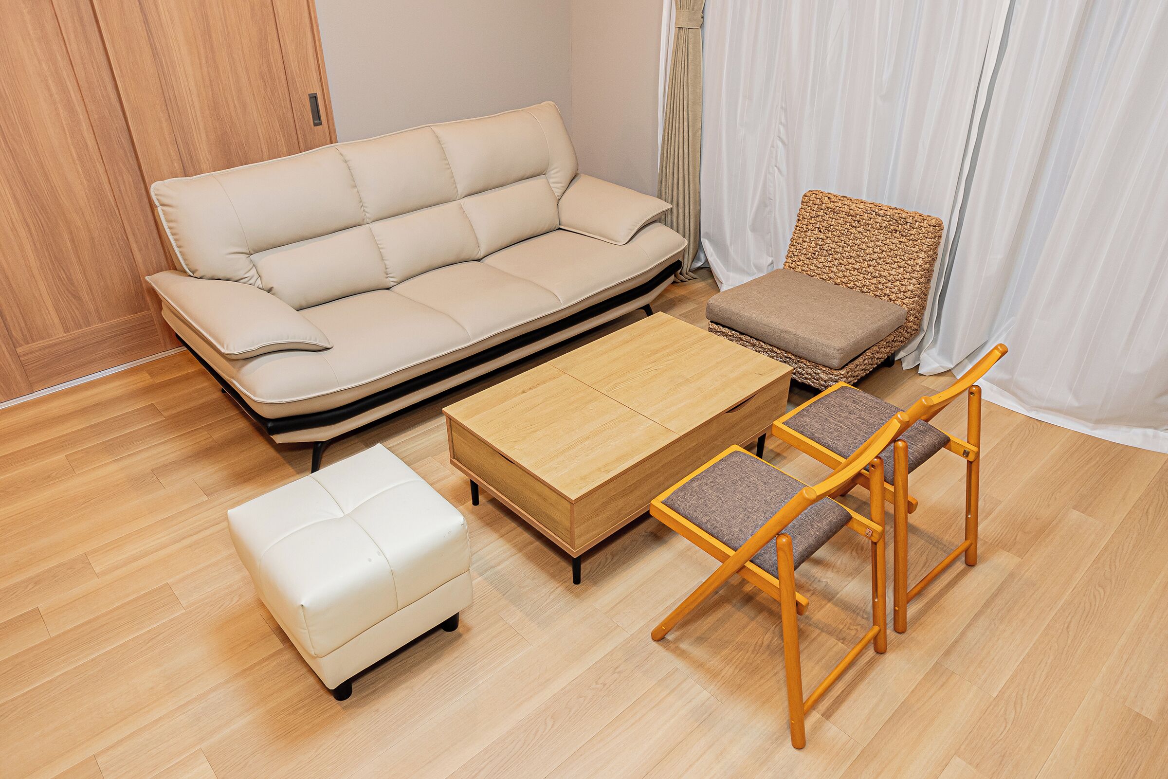 A room with a sofa, a small ottoman, a wooden coffee table, and a wicker chair.
