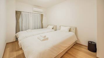 A hotel room with two beds, a waste bin, and an air conditioning unit.