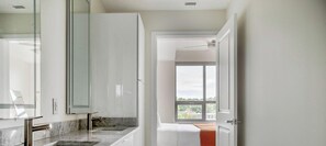 A modern bathroom with a glass shower enclosure, a marble countertop, and a view of the outdoors through a large window. - Blueground | Pentagon City, pool, nr Arlington Cemetery (Arlington)