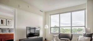 A modern living room with a large window, a flat-screen TV, a sofa, and a bed with a red blanket. - Blueground | Pentagon City, pool, nr Arlington Cemetery (Arlington)
