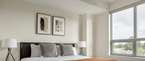 A hotel room with a bed, two bedside lamps, a window with a view, and two framed artworks on the wall. - Blueground | Pentagon City, pool, nr Arlington Cemetery (Arlington)