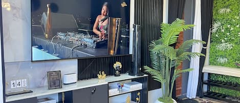 Una sala moderna con un televisor de pantalla plana grande, una mesa consola con adornos, una planta en maceta y vistas a zonas verdes al exterior.