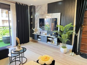 Una sala de estar moderna con un televisor de pantalla plana grande, un mueble multimedia negro, una mesa de centro de vidrio, un sofá cómodo y una planta en maceta.