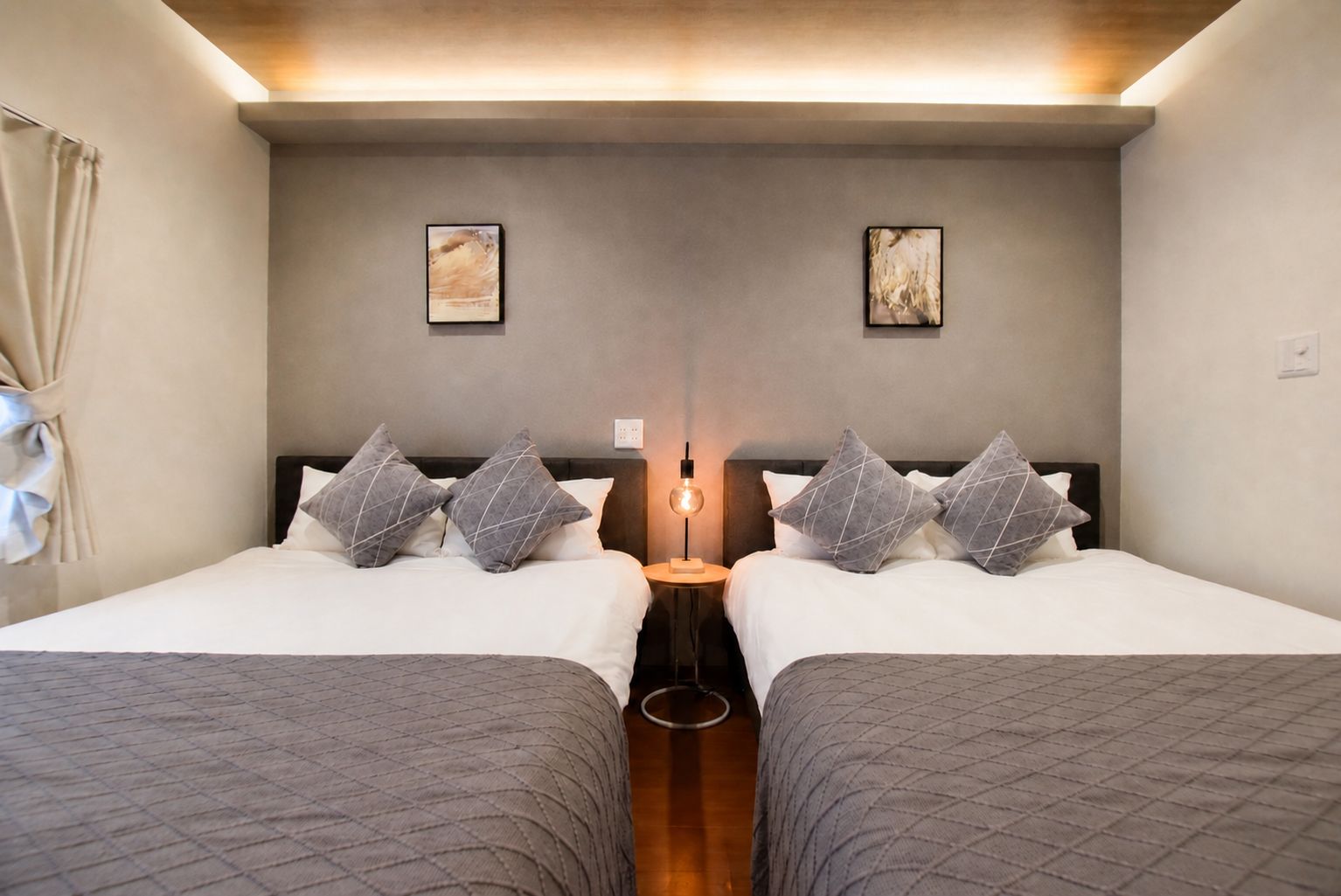A hotel room with two beds, a bedside table with a lamp, and artwork on the wall.