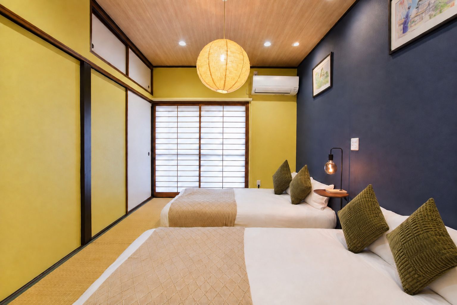 A hotel room with two beds, a large window with blinds, a hanging light fixture, and a wall-mounted air conditioner.