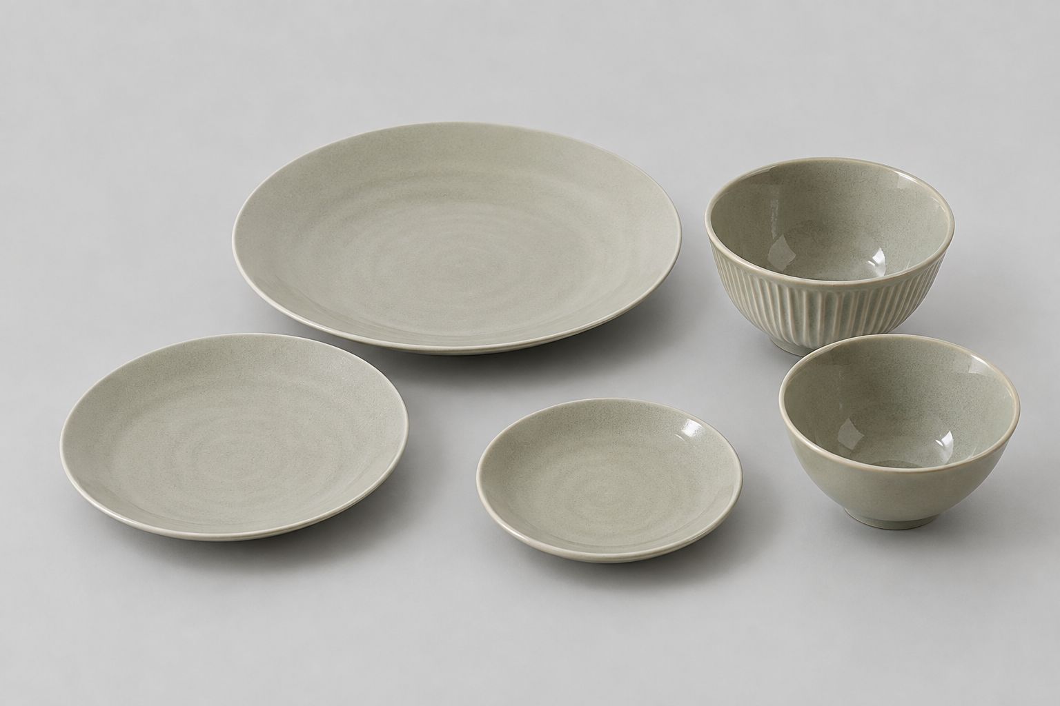 Ein Satz aus fünf Keramikschalen und Tellern mit glatter Oberfläche und heller Farbgebung.