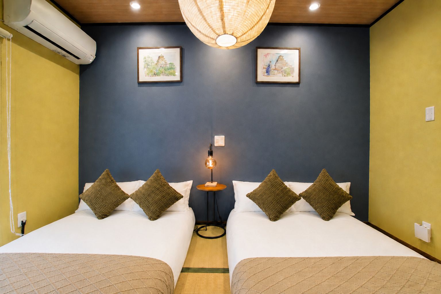 Une chambre d’hôtel avec deux lits, une table de chevet avec une lampe et des œuvres d’art accrochées au mur.