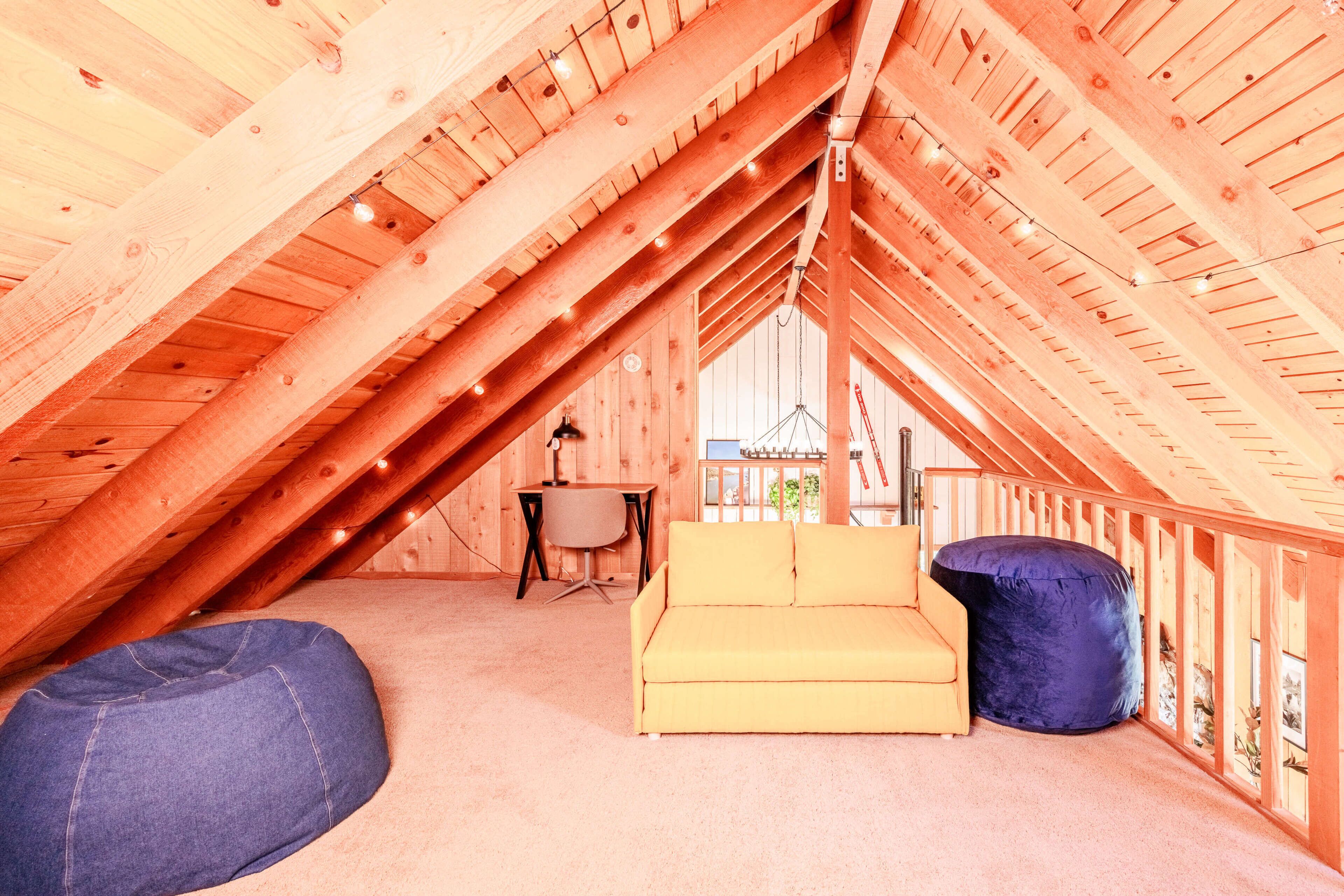 Une chambre mansardée avec un plafond en pente, un canapé jaune, un fauteuil en forme de poire bleu et un bureau avec une chaise.
