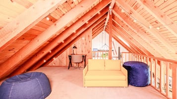 Une chambre mansardée avec un plafond en pente, un canapé jaune, un fauteuil en forme de poire bleu et un bureau avec une chaise.