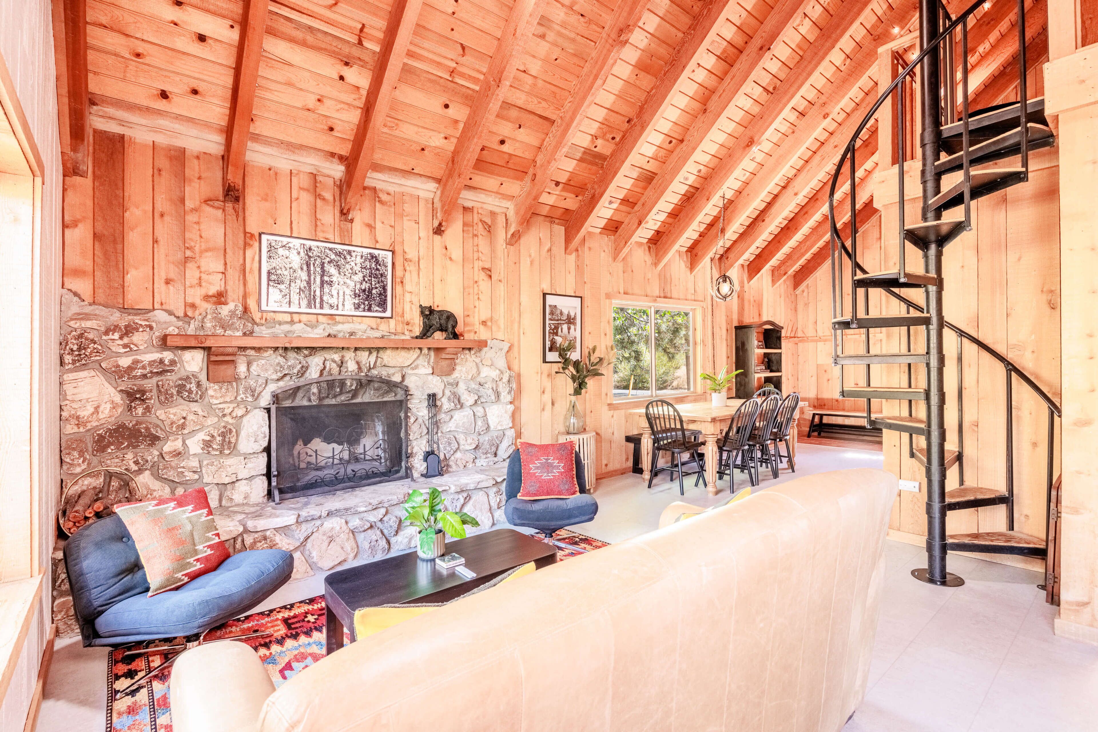 A wooden interior with a stone fireplace, seating area, and a staircase.