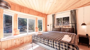 Quarto com cama, duas janelas, mesa de cabeceira e luminária suspensa.